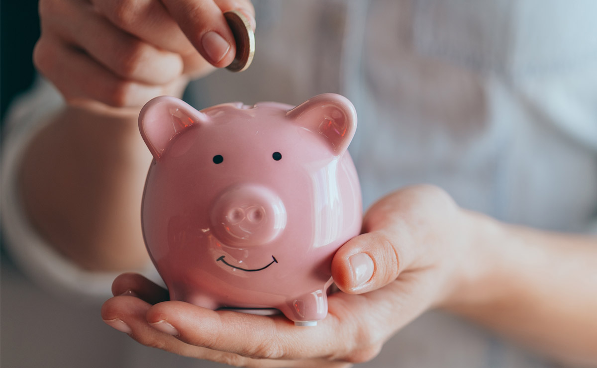 female hands hold a pink piggy bank and puts a coin into the top - saving money on HVAC costs
